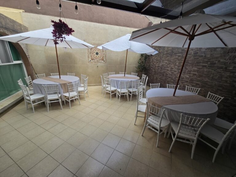 Mesas redondas, sillas blancas y sombrillas montadas en patio por Alquiladora Condesa en CDMX