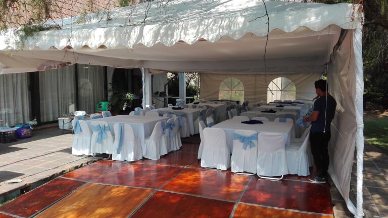 Carpa con piso de duela y mesas con manteles blancos y moños azules de Alquiladora Petit en CDMX